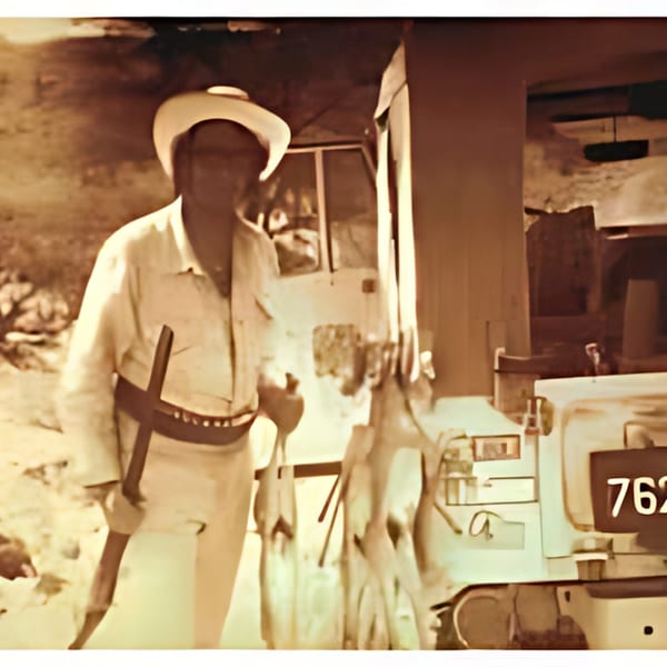 A man in a white hat and shirt, holding a tool, stands next to a vehicle.