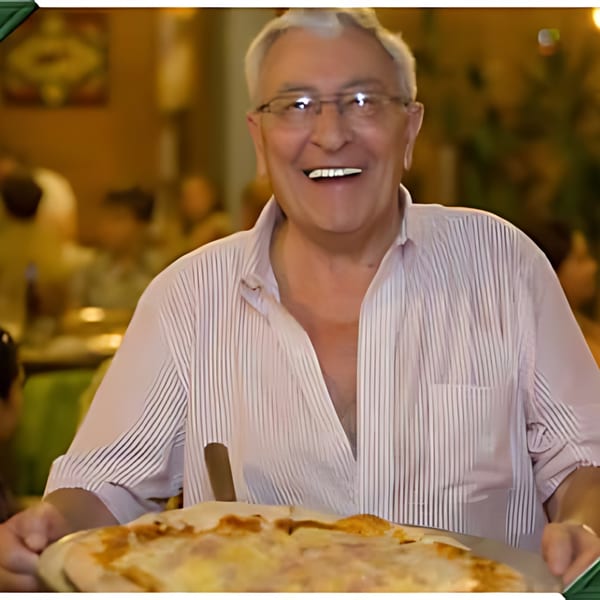Smiling man in glasses holding a fresh, hot pizza on a wooden peel at Mr. G's Pizzeria.