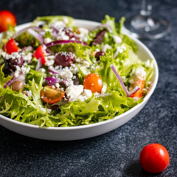 Fresh garden salad with lettuce, tomatoes, red onion, olives, and feta cheese in a white bowl.